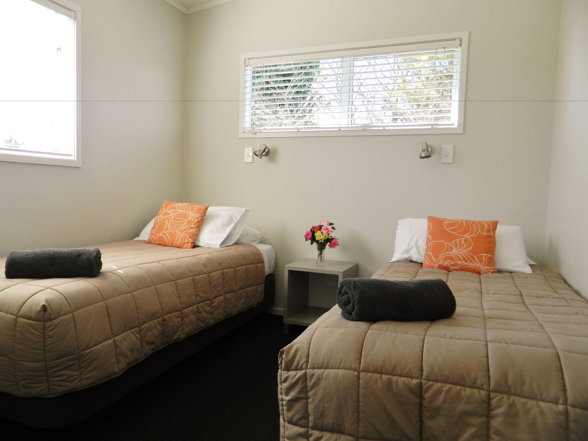 Taupo Debretts Spa Resort Екстериор снимка The image shows a small, cozy room featuring two single beds. Each bed is dressed with a beige quilt and has an orange decorative pillow. There are two rolled towels placed on the beds. A small bedside table is located between the beds, with a vase o