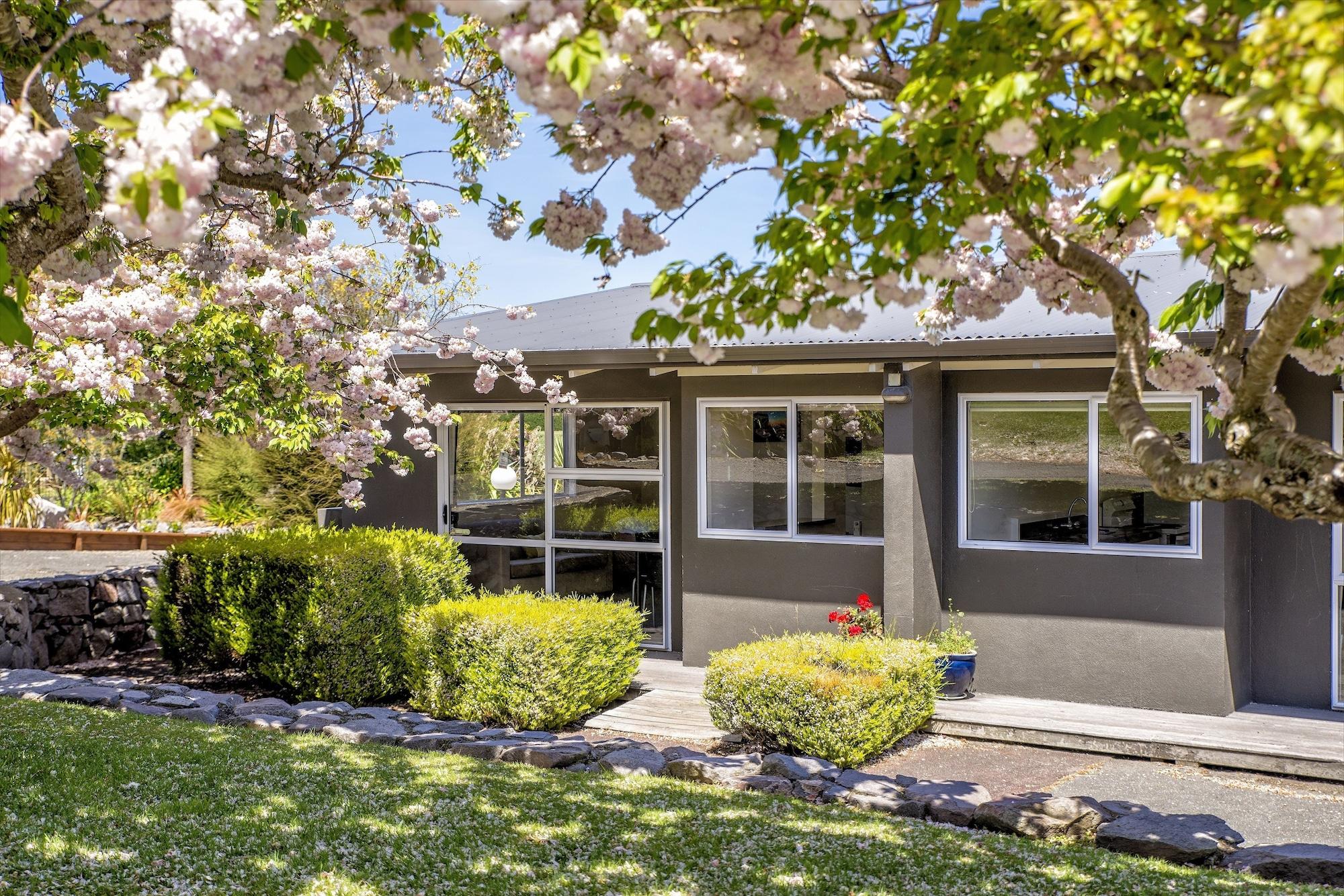 Taupo Debretts Spa Resort Екстериор снимка The photo shows a charming house surrounded by vibrant greenery and blooming trees. There are pink flowers from the trees adding a pop of color to the scene. The house features large windows that allow natural light to fill the interior. A well-maint