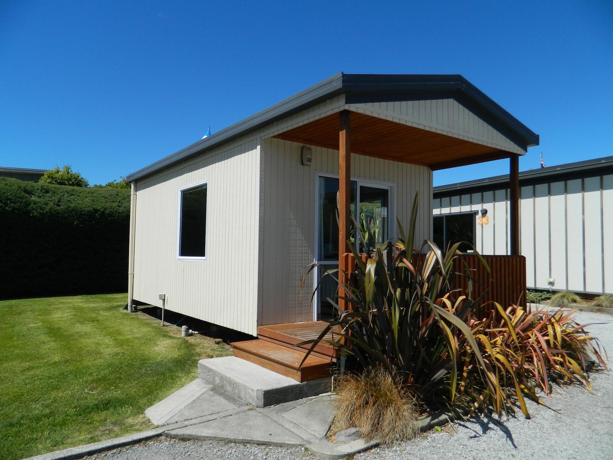 Taupo Debretts Spa Resort Екстериор снимка The photo shows a small, modern cabin or vacation home. It features a light-colored exterior with a a small porch at the entrance. The porch has wooden steps that lead up to the front door. Surrounding the cabin is a neat lawn, with some landscaping 
