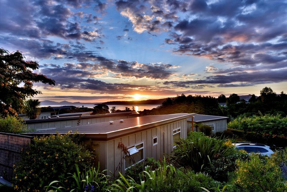 Taupo Debretts Spa Resort Екстериор снимка The photo depicts a serene landscape during sunset. In the foreground, there is a modest building partially covered by greenery. The roof of the building is visible, along with some windows. Surrounding the structure are lush plants and foliage. 

In