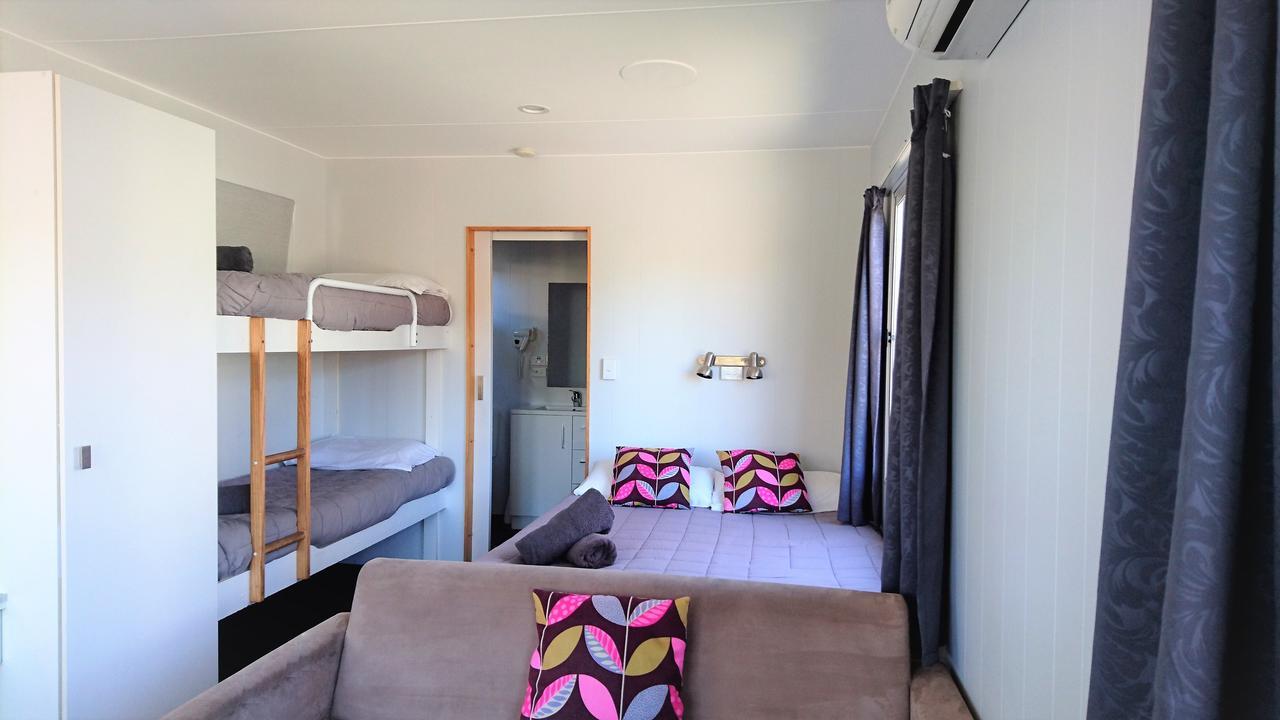 Taupo Debretts Spa Resort Екстериор снимка The photo shows a cozy interior of a room. On the left, there is a bunk bed with two levels, each with gray bedding. In the middle, there is a doorway leading to another space, which appears to be a bathroom. To the right, there is a comfortable couc