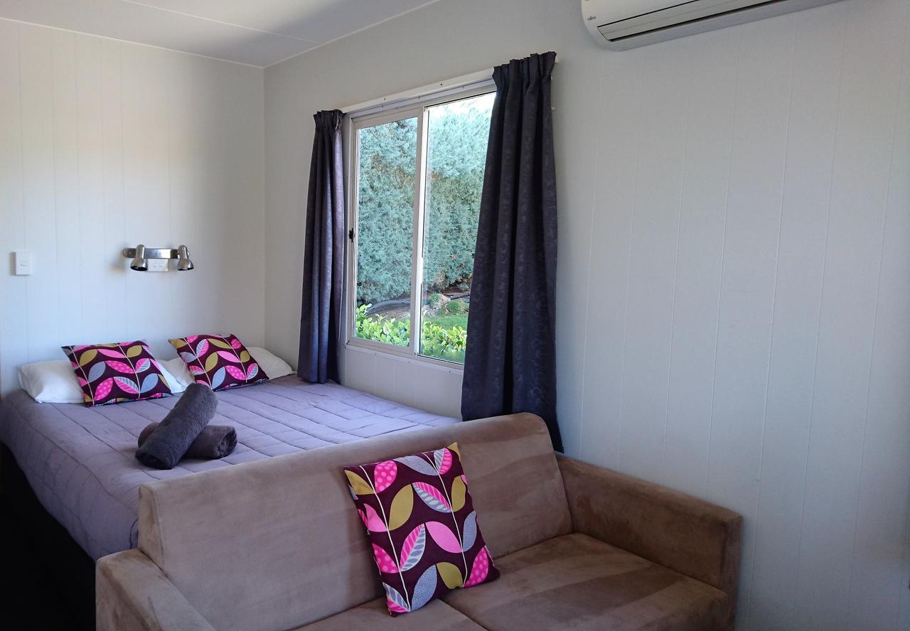 Taupo Debretts Spa Resort Екстериор снимка The photo shows a cozy room featuring a bed with colorful patterned cushions and a brown sofa. There are two large windows with dark curtains, allowing natural light to brighten the space. The walls are painted in a light color, and there are some pl