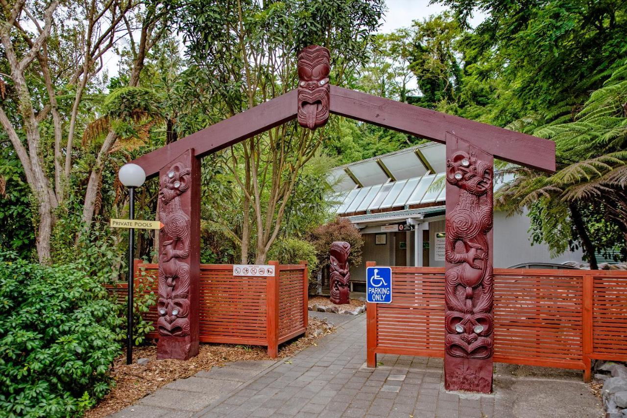 Taupo Debretts Spa Resort Екстериор снимка The photo shows an entrance with a large archway that features intricate carvings. The arch is supported by two vertical posts, each adorned with detailed figures likely representing cultural symbols or characters. Surrounding the entrance are lush g