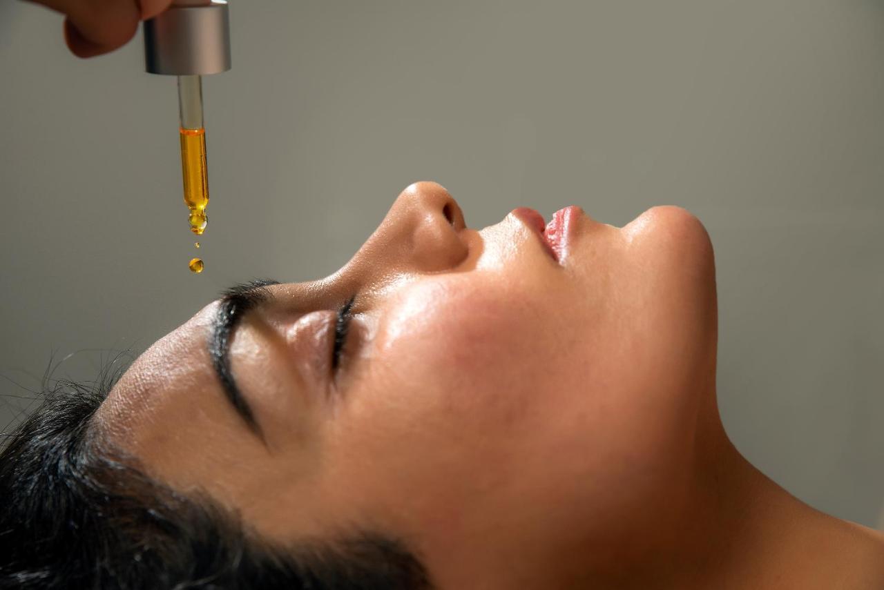 Taupo Debretts Spa Resort Екстериор снимка The image shows a close-up of a woman's face as she lies back, eyes closed. A dropper is held above her forehead, with a drop of an oil or serum about to fall. The woman's skin appears radiant and moist, indicating a skincare treatment, possibly focu