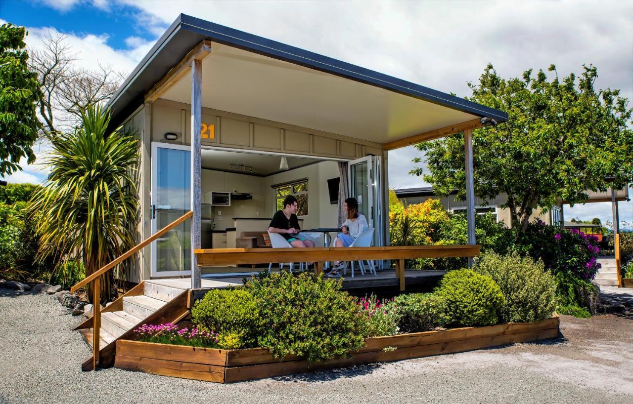 Taupo Debretts Spa Resort Екстериор снимка The photo depicts a modern small house or cabin, featuring a covered porch with a wooden railing. Two people are seated at a table on the porch, engaging in conversation. The exterior of the house is designed with large windows, allowing ample natura